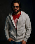 Man wearing a gray hoodie over a red shirt with sunglasses on a dark background