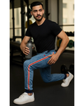 Man in black t-shirt and blue jeans with red stripes holding a water bottle in a gym setting