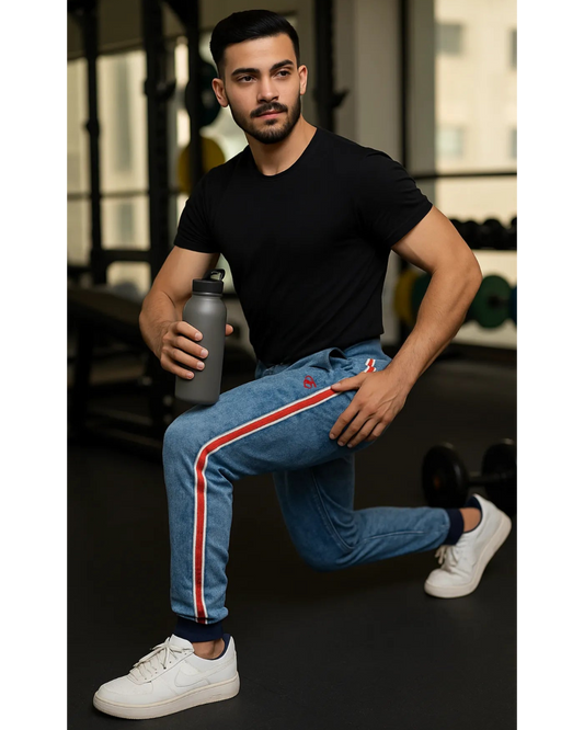 Man in black t-shirt and blue jeans with red stripes holding a water bottle in a gym setting