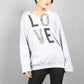 Person wearing a light gray sweatshirt with 'LOVE' printed on it against a plain background