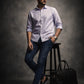 Man in light shirt and dark jeans standing next to a black bag on a gray background