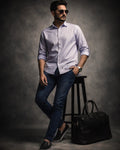 Man in light shirt and dark jeans standing next to a black bag on a gray background