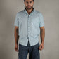 Man wearing a light blue shirt and dark shorts against a wooden background