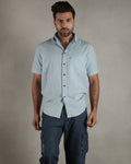 Man wearing a light blue shirt and dark shorts against a wooden background