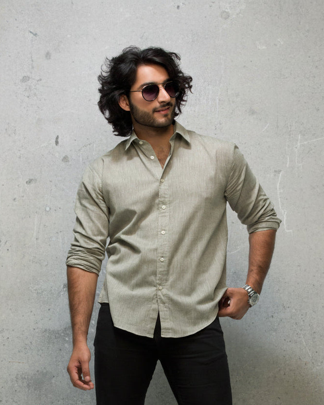 Man wearing a light olive  shirt and sunglasses against a white background