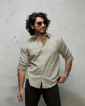 Man wearing a light olive  shirt and sunglasses against a white background