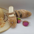Decorative sandal with embellishments, a straw hat, and colorful sunglasses on a light background