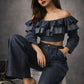 Woman wearing a dark blue ruffled top and pants sitting on a chair against a gray background