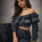 Woman wearing a dark denim off-shoulder top and jeans against a gray background