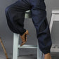 Person wearing dark blue pants sitting on a white stool against a gray background