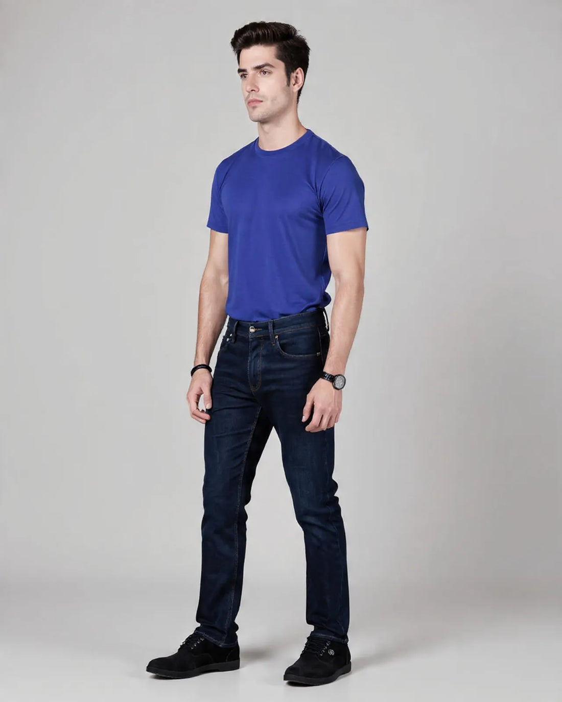 Man wearing a blue t-shirt and dark jeans on a gray background