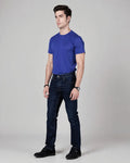 Man wearing a blue t-shirt and dark jeans on a gray background