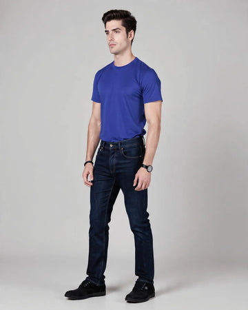 Man wearing a blue t-shirt and dark jeans on a gray background