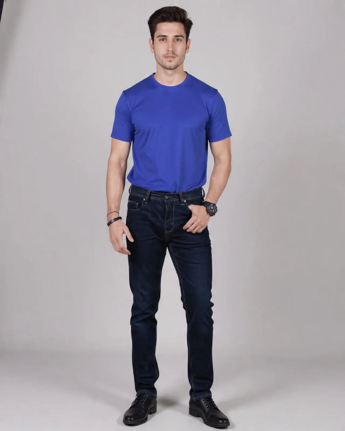Man wearing a blue t-shirt and dark jeans on a gray background