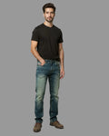 Man wearing a black t-shirt and blue jeans against a gray background