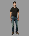 Man wearing a black t-shirt and blue jeans against a gray background