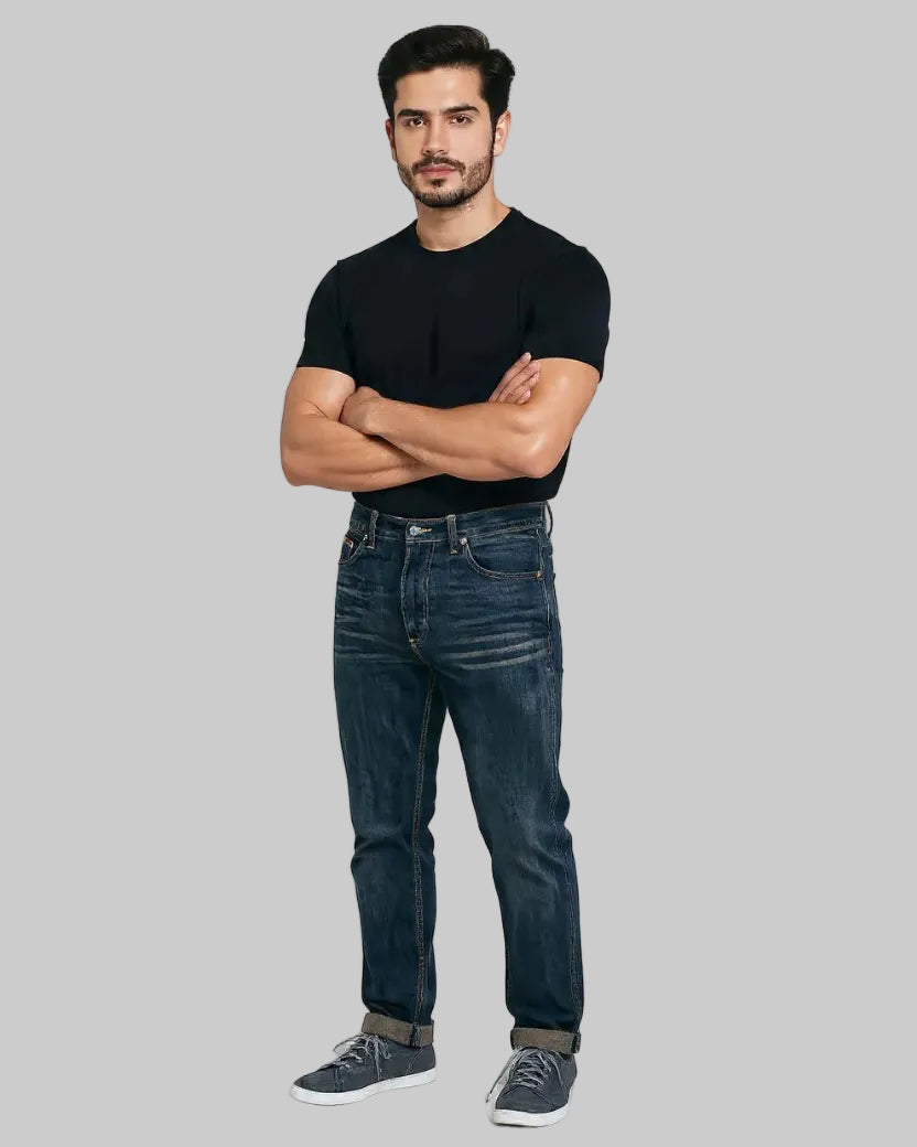 Man wearing a black t-shirt and blue jeans standing against a white background