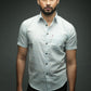 Man wearing a light gray button-up shirt against a dark background