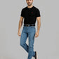 Man wearing a black t-shirt with a red logo and blue jeans on a gray background