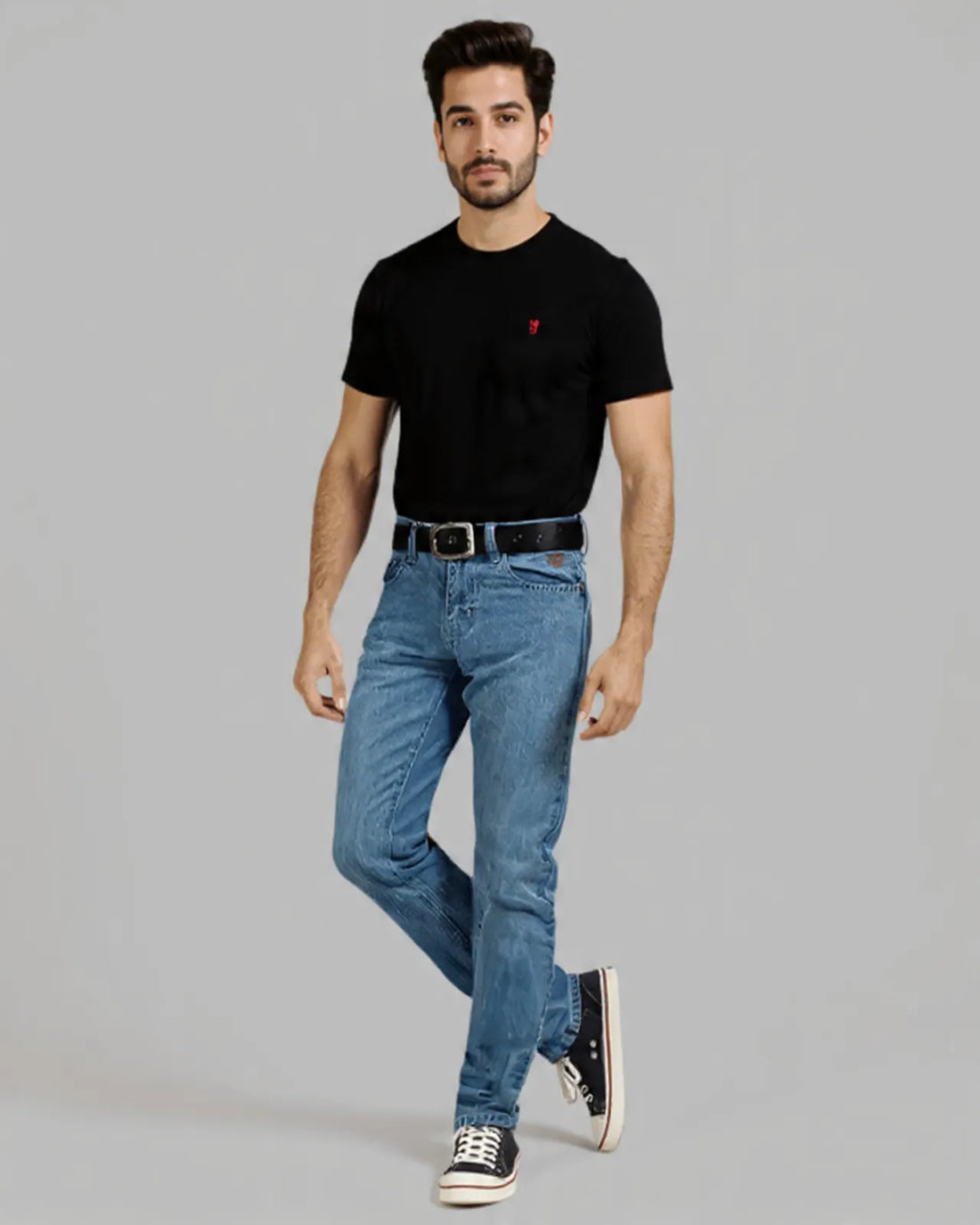 Man wearing a black t-shirt with a red logo and blue jeans on a gray background
