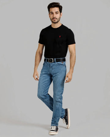 Man wearing a black t-shirt with a red logo and blue jeans on a gray background