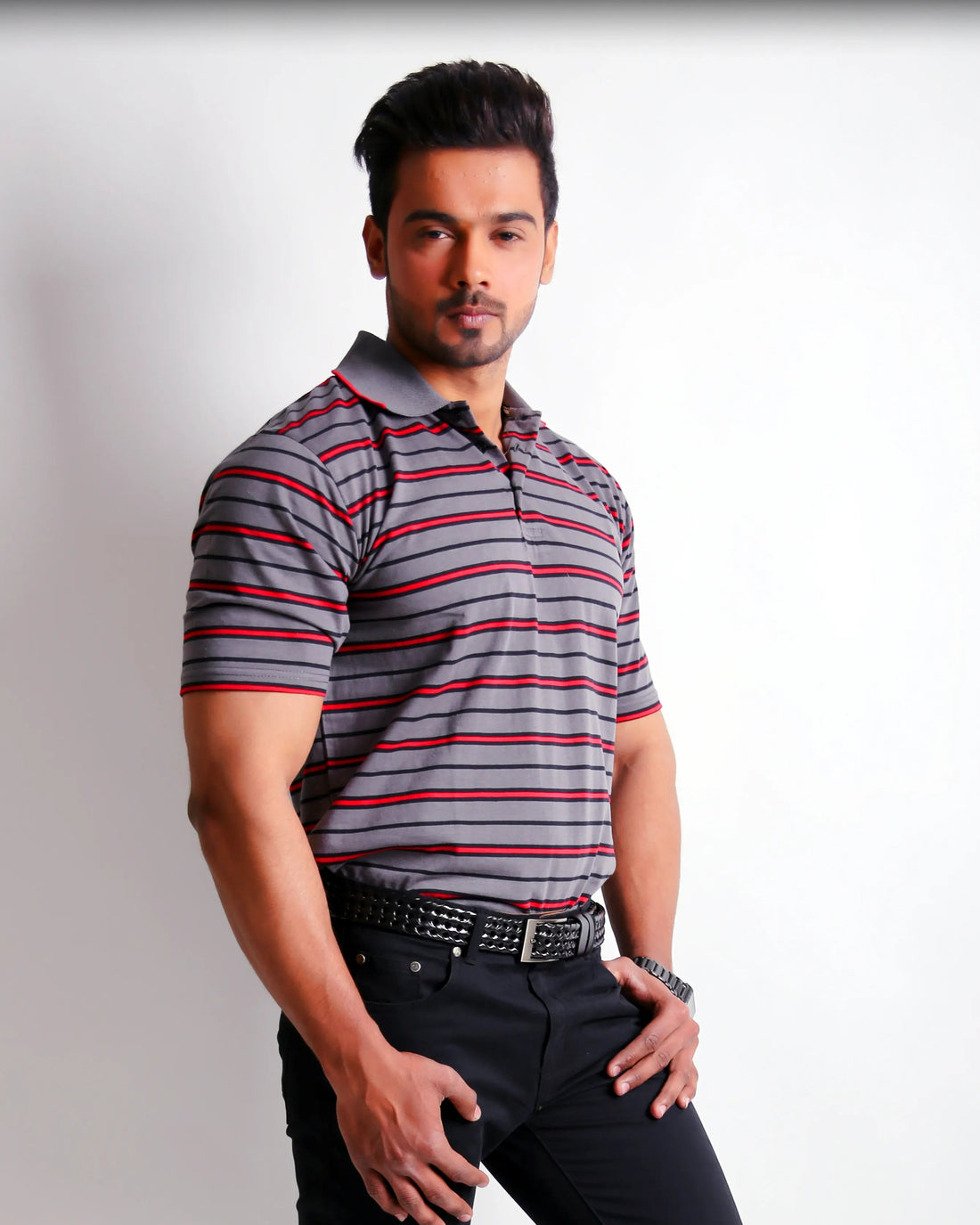 Man wearing a striped polo shirt and dark jeans on a white background