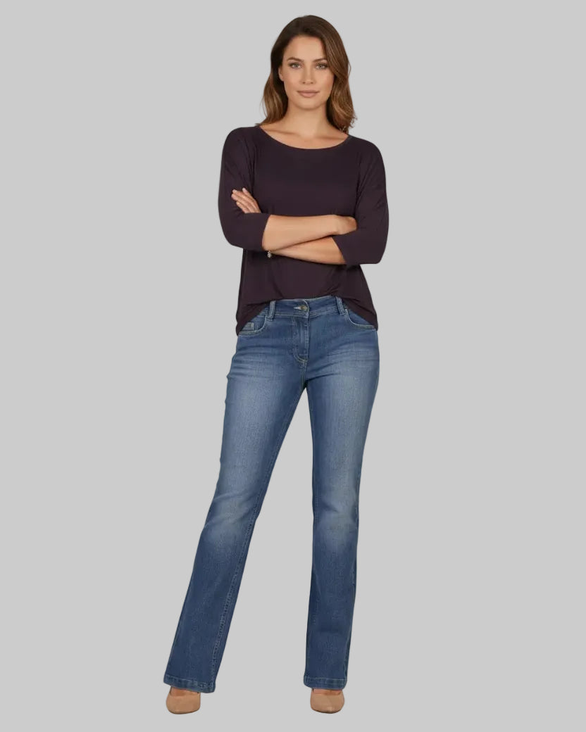 Woman wearing a dark purple sweater and blue jeans on a white background
