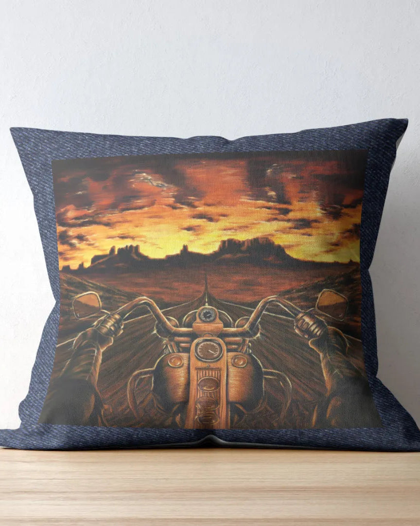 Decorative pillow with a motorcycle and sunset design on a wooden surface.