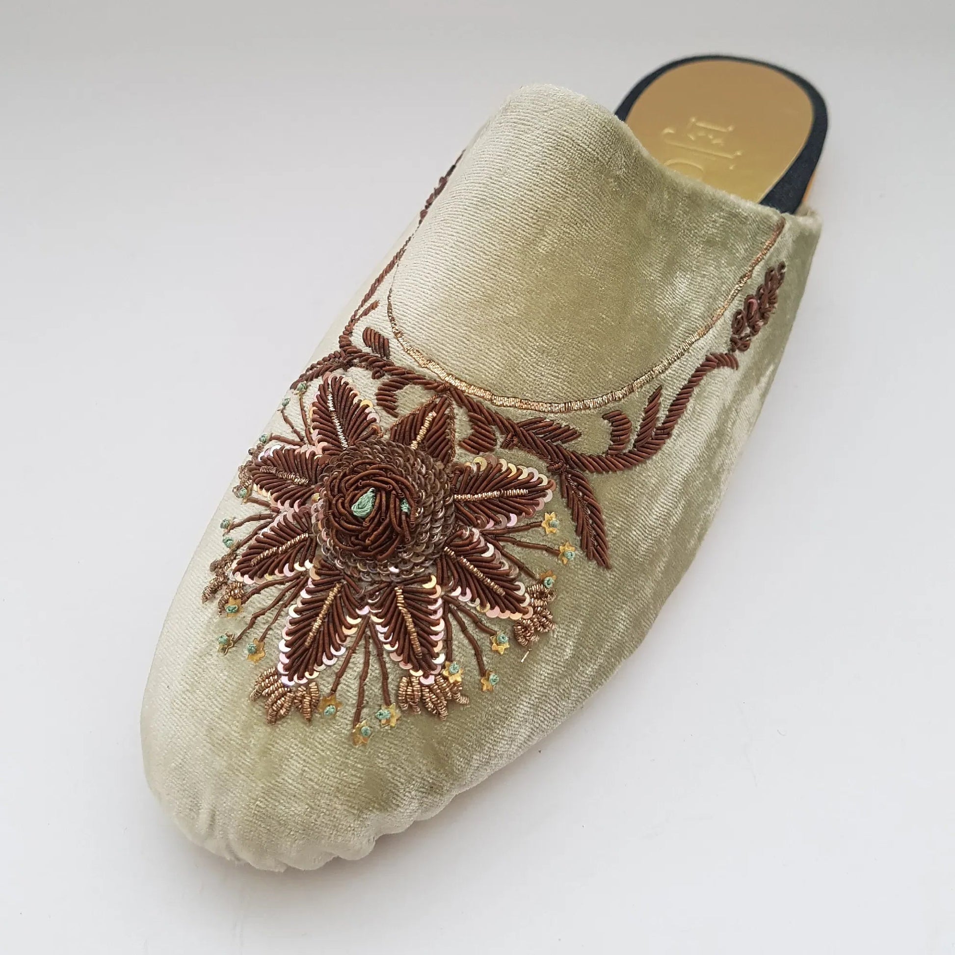 Beige slipper with brown floral embroidery on a light gray background