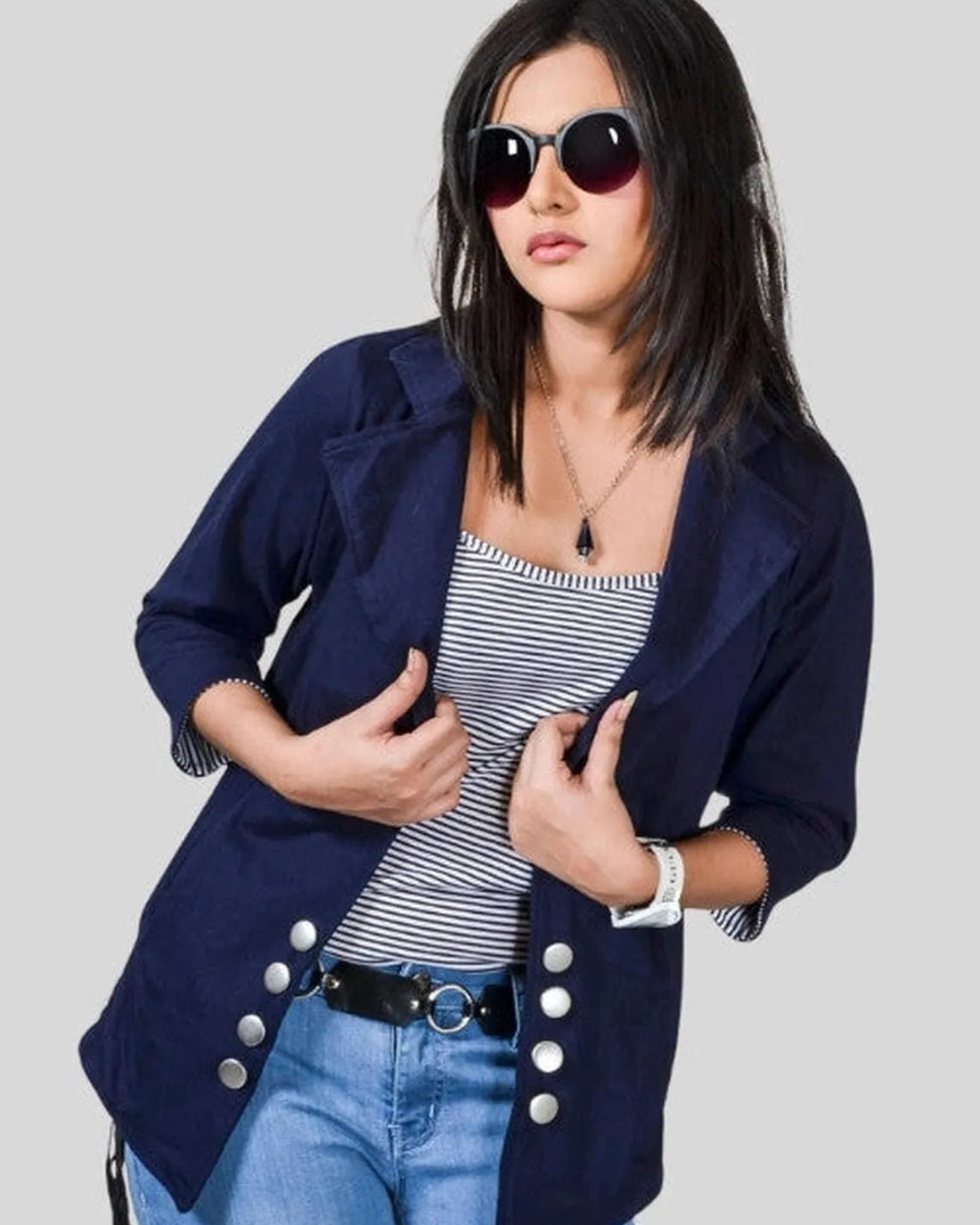 Woman wearing a navy blazer, striped top, and blue jeans on a plain background