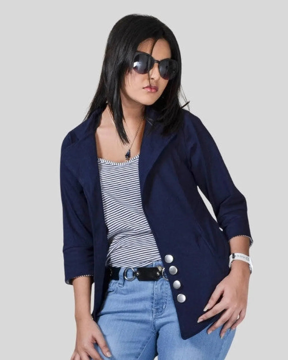 Woman wearing a navy blazer, striped top, and blue jeans on a plain background