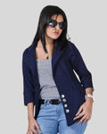 Woman wearing a navy blazer, striped top, and blue jeans on a plain background