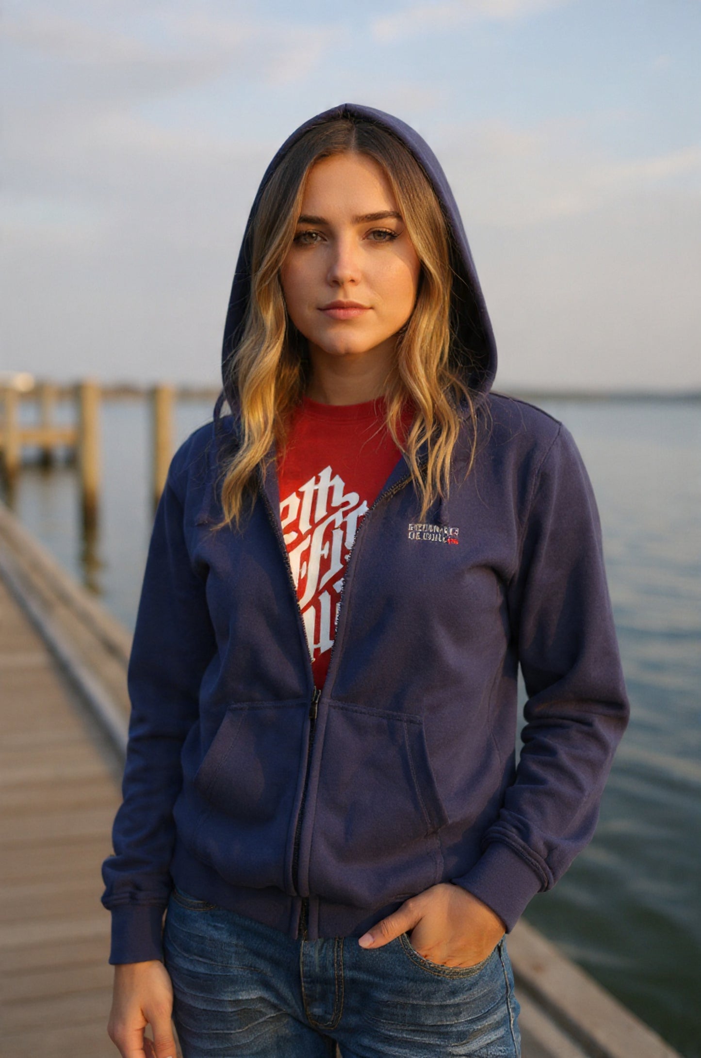 Person wearing a blue hoodie with a logo on a dock by water