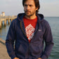 Man wearing a navy blue hoodie with a red shirt underneath, standing by a waterfront.
