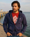 Man wearing a navy blue hoodie with a red shirt underneath, standing by a waterfront.