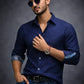 Man wearing a navy blue shirt with rolled-up sleeves against a dark background