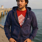 Man wearing a navy blue hoodie with a red shirt underneath, standing by a waterfront.