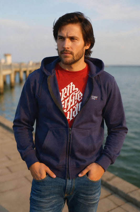 Man wearing a navy blue hoodie with a red shirt underneath, standing by a waterfront.