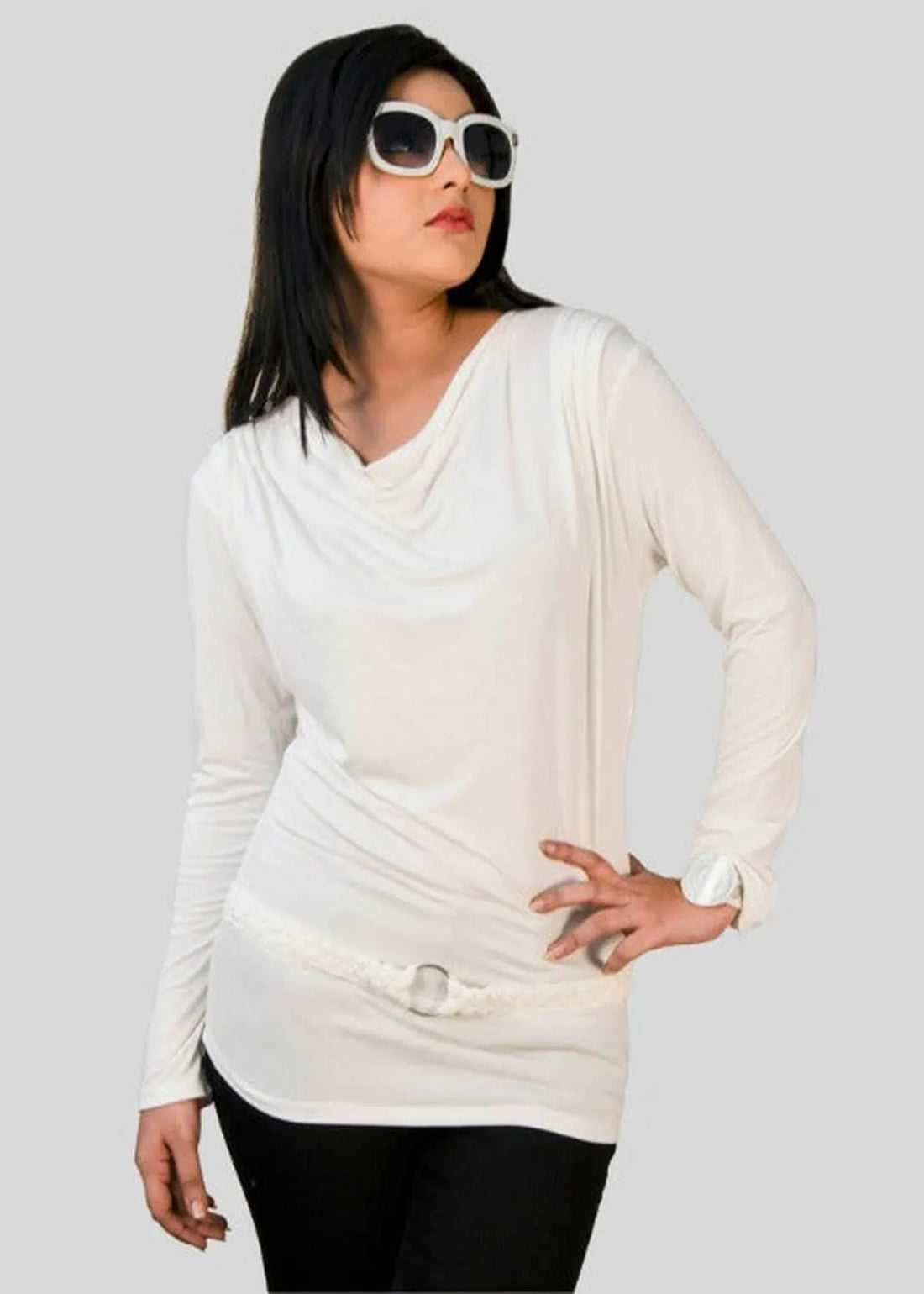 Woman wearing a white long-sleeve top and sunglasses on a plain background
