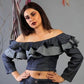 Woman wearing a dark blue off-shoulder top with ruffles against a gray background