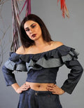 Woman wearing a dark blue off-shoulder top with ruffles against a gray background