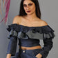 Woman wearing a dark blue off-shoulder top with ruffles against a gray background