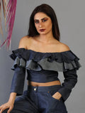 Woman wearing a dark blue off-shoulder top with ruffles against a gray background