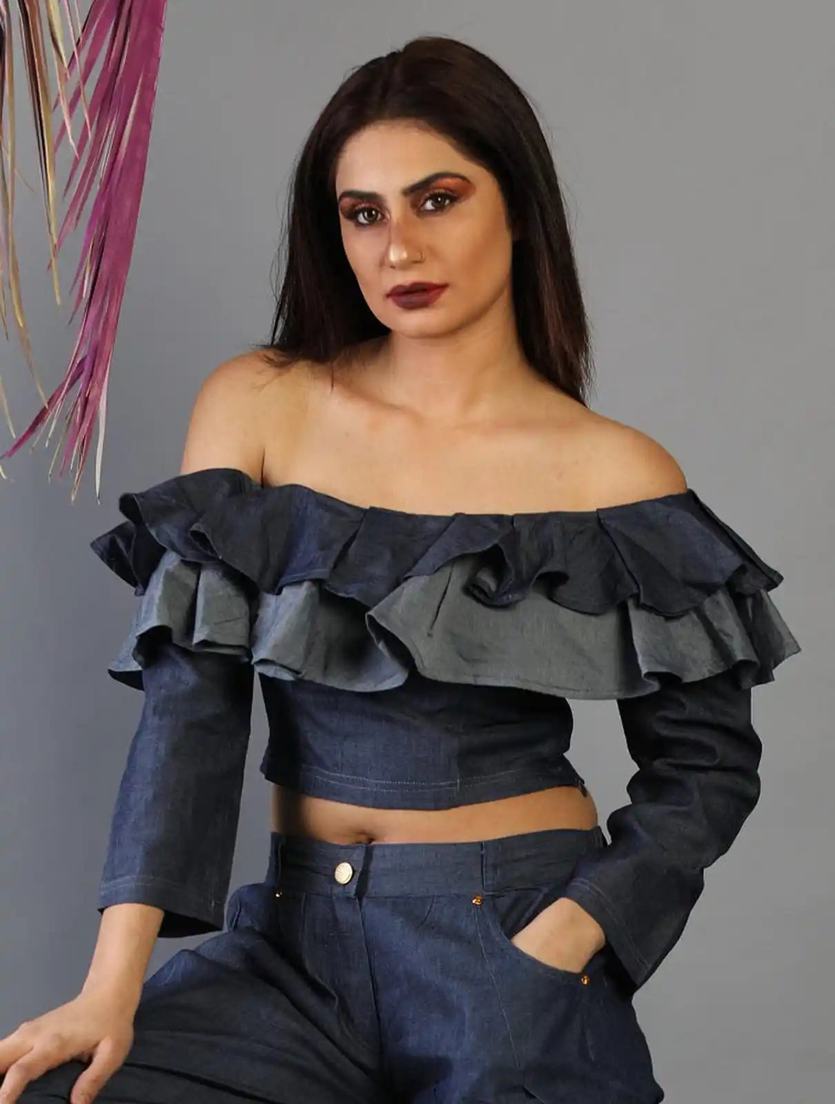 Woman wearing a dark blue off-shoulder top with ruffles against a gray background
