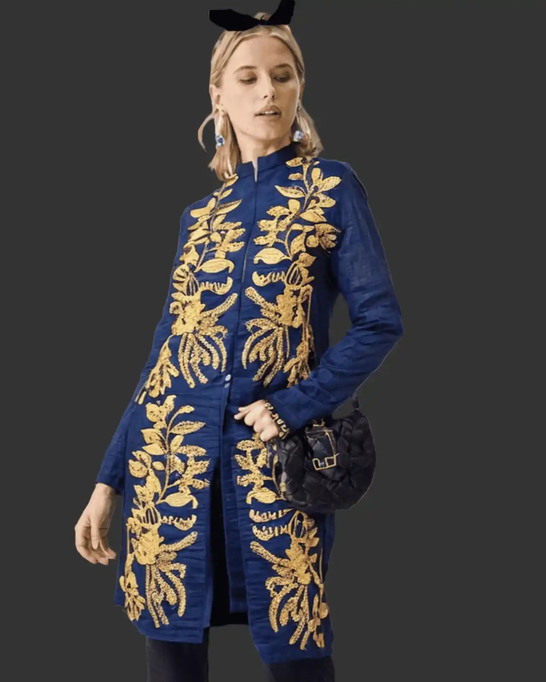 Woman wearing a blue embroidered coat with gold patterns on a black background