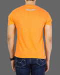 Person wearing an orange t-shirt with a logo on the back, standing against a gray background