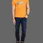 Person wearing an orange t-shirt with a logo and dark blue jeans on a gray background