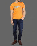 Person wearing an orange t-shirt with a logo and dark blue jeans on a gray background