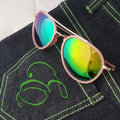 Sunglasses with green and blue reflective lenses on a dark denim fabric background