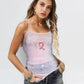Woman wearing a light purple tank top with a pink ribbon design on a plain background